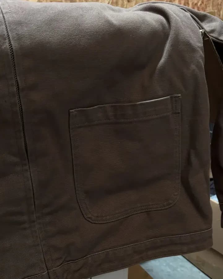 Close-up of a brown canvas work jacket with a patch pocket.
