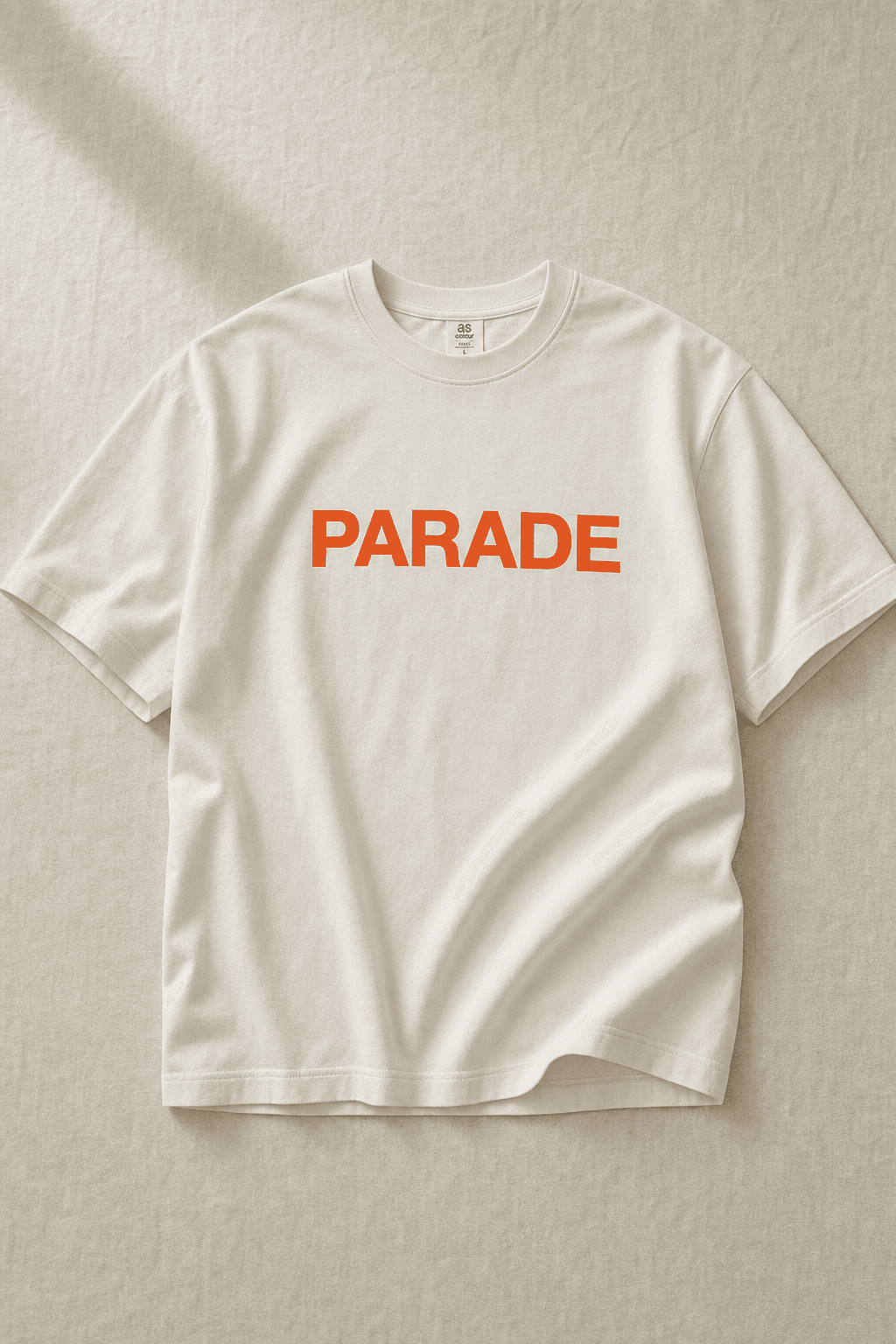 Bone-white heavyweight tee with bold signal-orange PARADE chest graphic — the kind of product an operator can sell from their ThreadzShops store.